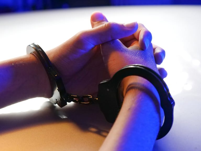 Close-up of handcuffed hands under blue police light, signifying arrest or detention.