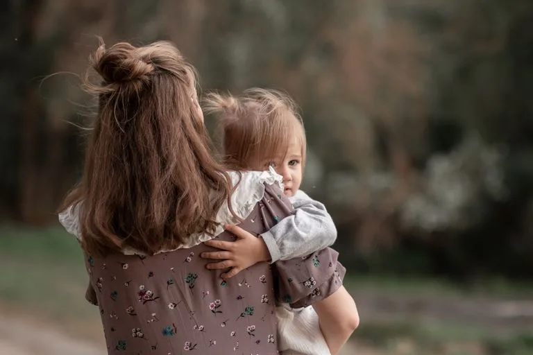 A tender outdoor moment of a mother holding her daughter in serene surroundings.